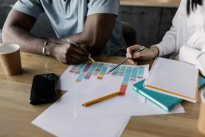 Mains esquissant des idées de produits et des diagrammes de marché sur un bureau avec des notes et des carnets