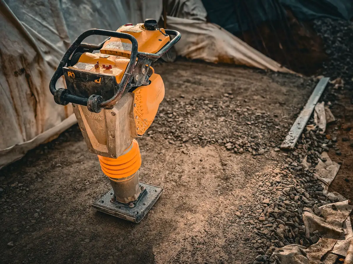 Outils de préparation du sol : pelle, niveau et plaque vibrante sur un chantier