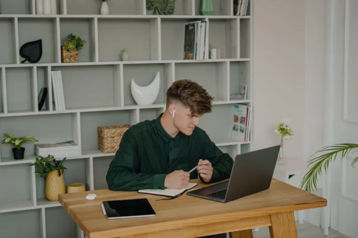 Personne étudiant l'allemand en ligne avec un ordinateur portable, un carnet et un casque sur son bureau