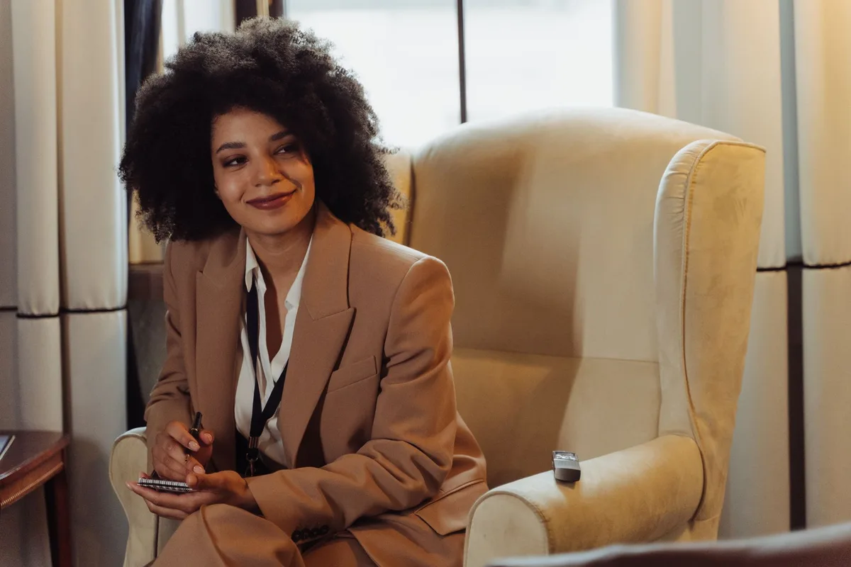 Femme en tenue professionnelle souriante, posture ouverte, établissant un contact visuel bienveillant.
