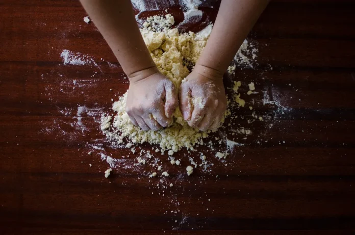 Mains pétrissant la pâte sur un plan de travail enfariné avec outils de boulangerie