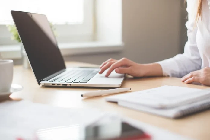 Bureau en journée avec ordinateur, carnet ouvert et mains triant des notes