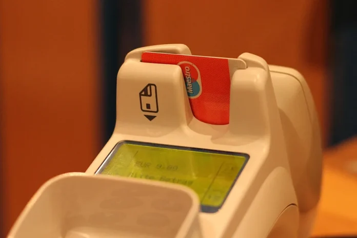 Client approchant un smartphone d'un terminal de paiement sur un comptoir en boutique, en plein jour